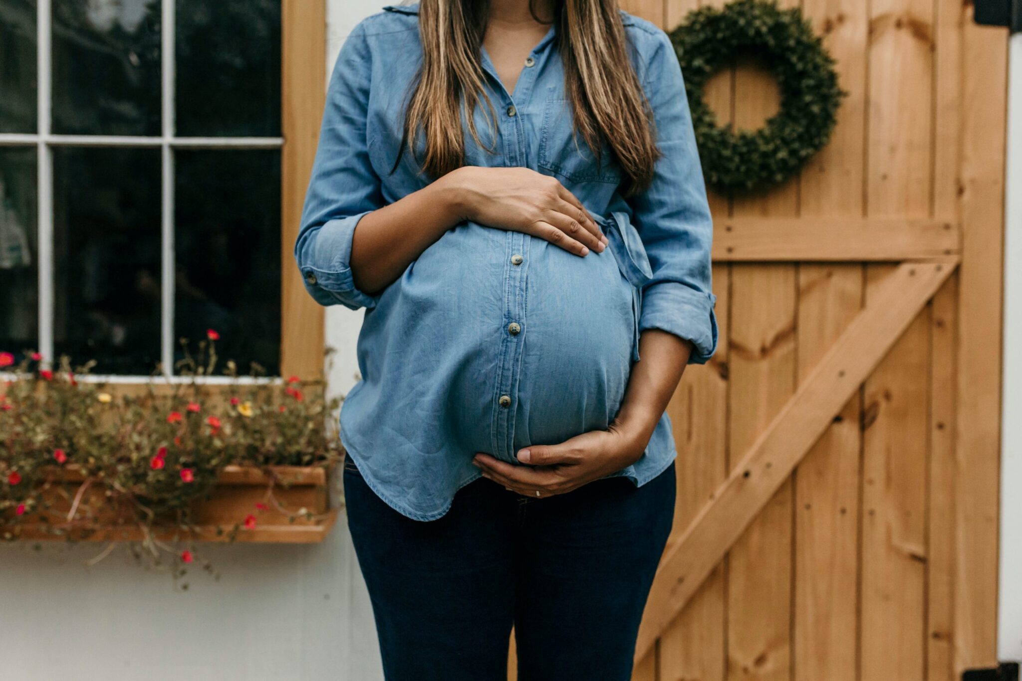 Pregnant woman holding her stomach and standing in front of wooden house