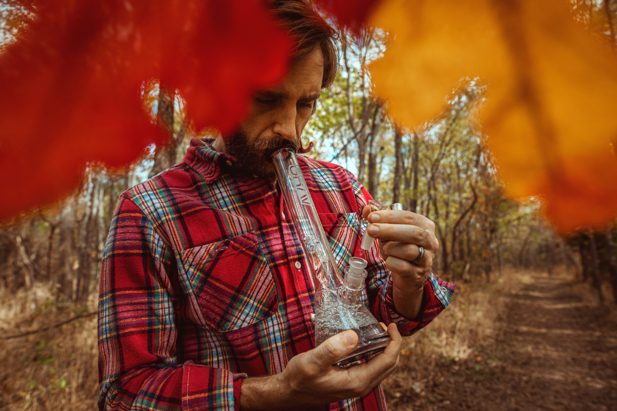 Man hitting a bong correctly in a colorful forest.