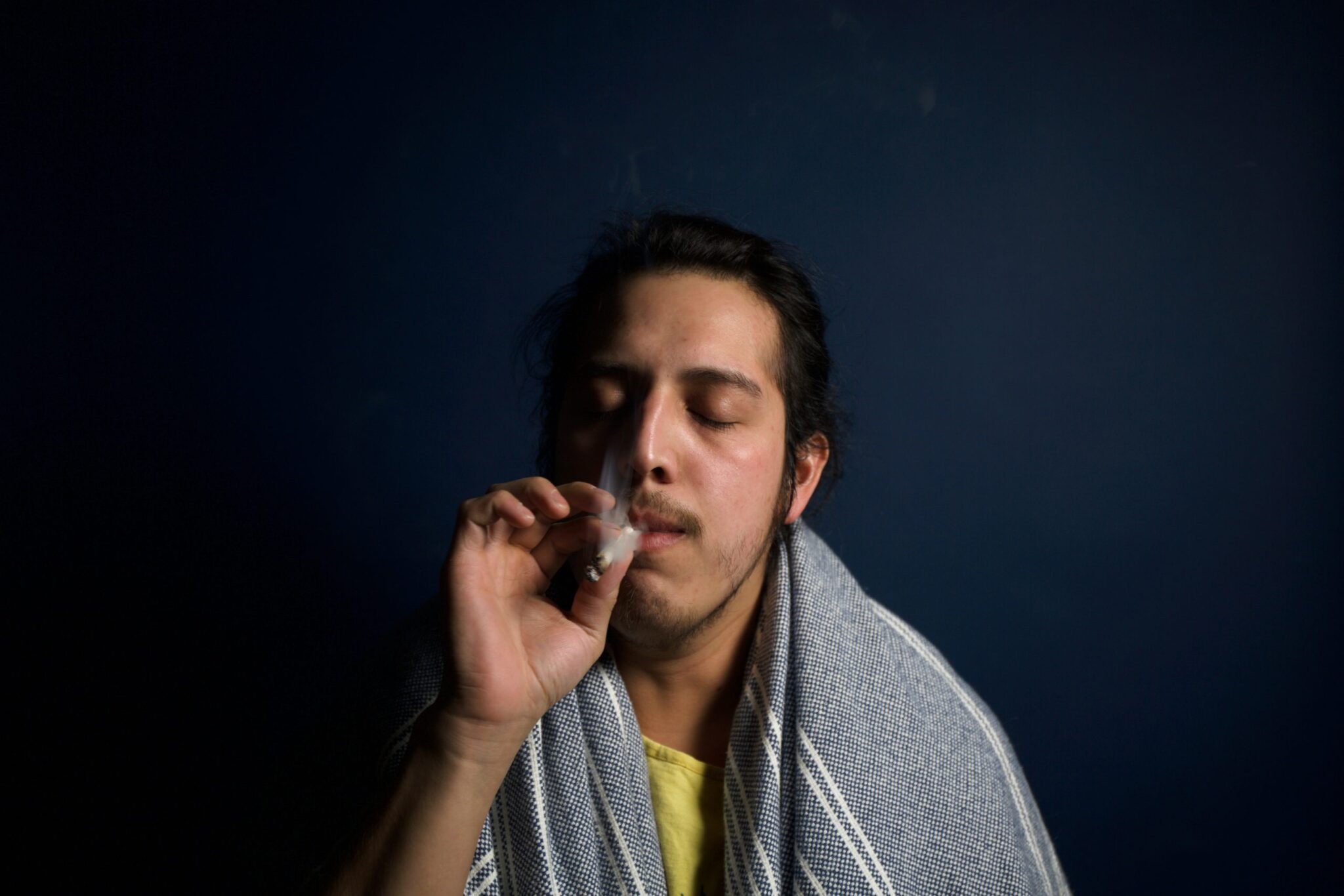 man covered with a blanket smoking a joint